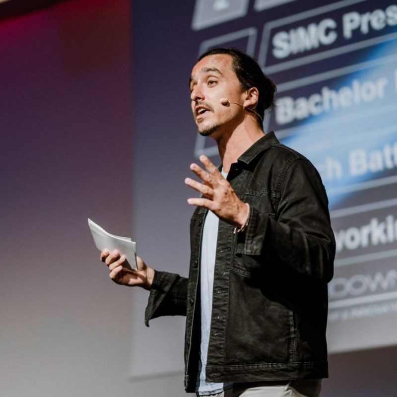 James Langer speaking on stage with a headset microphone